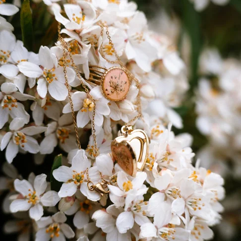 Bijoux en fleurs séchées clermont - Médaillon doré en forme de coeur, en fleurs de carotte sauvage sur un fond pêche.