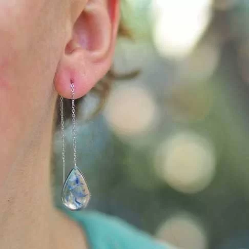 Boucle d'oreille goutte en acier inoxydable avec inclusion de fleurs de bleuet portée sur une oreille - bijou fleur