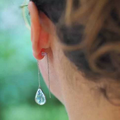 Boucle d'oreille goutte en acier inoxydable avec inclusion de fleurs de bleuet portée sur une oreille