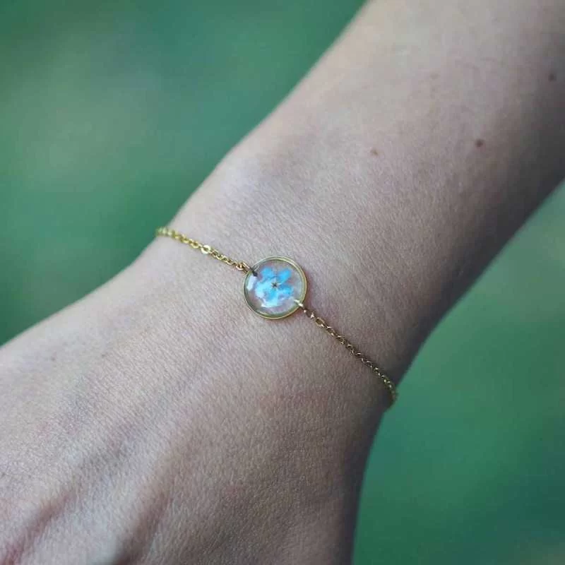 Bracelet doré avec inclusion de fleur de myosotis bleu porté au poignet - bijou fleur