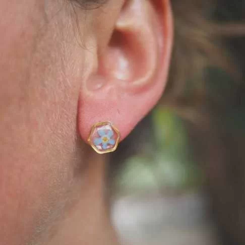 Puces d'oreille dorées avec inclusion de fleur de myosotis bleu sur fond de résine transparente portées à l'oreille