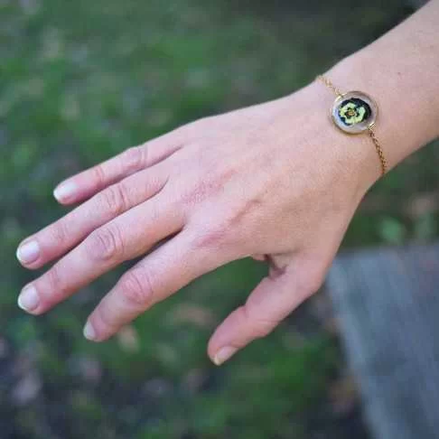 Bracelet rond en acier inoxydable doré avec inclusion de fleur de pensée dans de la résine transparente porté - bijou fleur