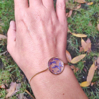 bracelet doré avec inclusion de fleurs de bleuet porté sur un poignet - bijou fleur