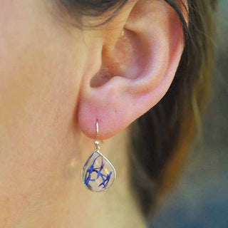 Boucle d'oreille petite goutte en laiton doré à l'or fin avec inclusion de fleurs de bleuet portée  sur une oreille