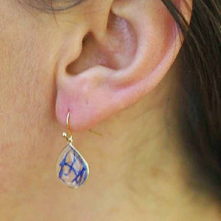 Boucle d'oreille petite goutte en laiton doré à l'or fin avec inclusion de fleurs de bleuet portée  sur une oreille