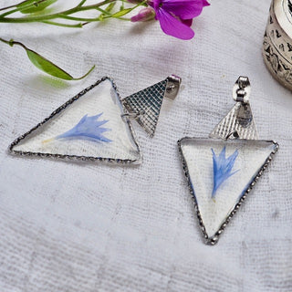 bijou fleur - Boucles d'oreille argentées en forme de  triangle avec inclusion d'une fleur de bleuet bleue sur fond blanc