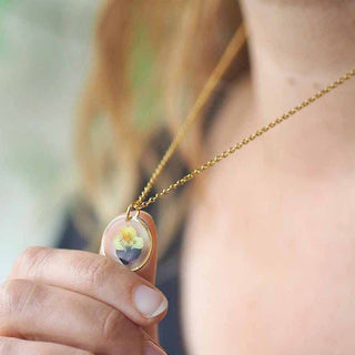 Collier en acier inoxydable doré avec inclusion de fleur de pensée dans de la résine transparente porté