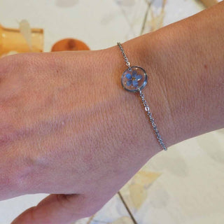 Bracelet argenté avec inclusion de fleur de myosotis bleu porté au poignet - bijou fleur