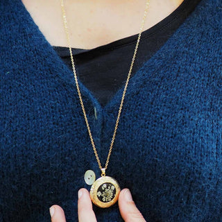 Sautoir en acier inoxydable doré avec inclusion de fleur de carotte sauvage dans de la résine noire porté - collier fleur