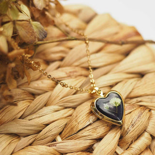 Médaillon doré en forme de coeur avec inclusion d'une fleur de gypsophile blanche dans de la résine noire - collier fleur