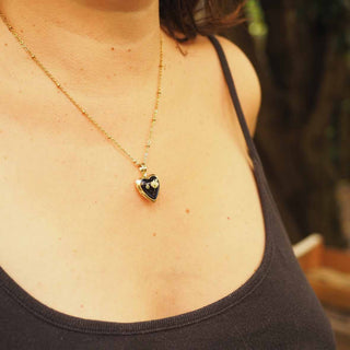 Médaillon doré en forme de coeur avec inclusion d'une fleur de gypsophile blanche dans de la résine noire porté autour du cou