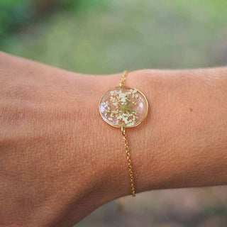 Bracelet rond en acier inoxydable doré avec inclusion de fleur de carotte sauvage dans de la résine transparente au poignet